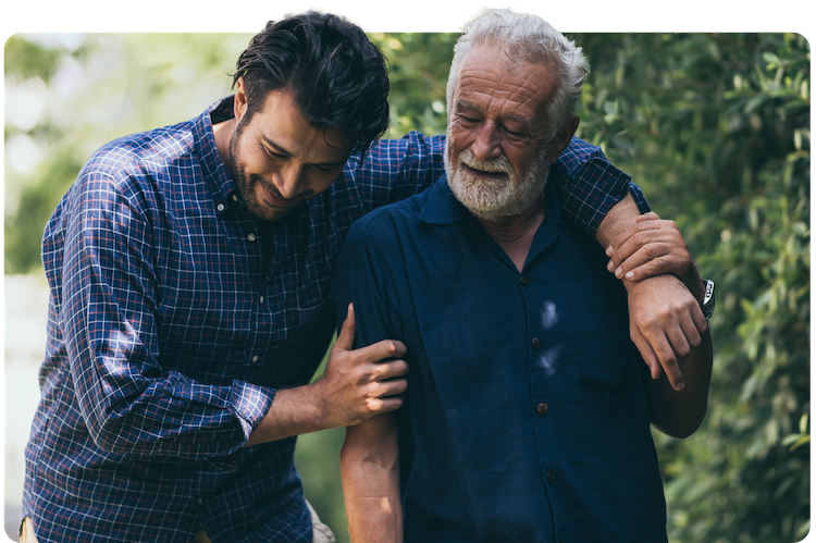 The old man and his son are walking in the park. A man hugs his elderly father. They are happy and smiling